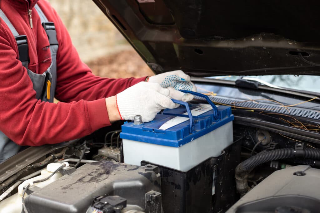 Cropped image of a car mechanic placing a car battery back into the car